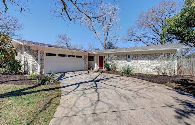 view of front of property featuring a garage, stone siding, driveway, and fence