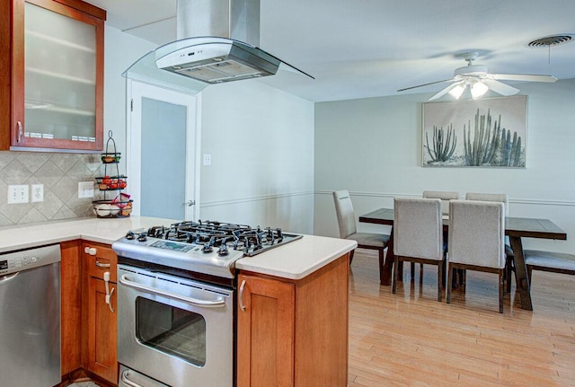 kitchen featuring appliances with stainless steel finishes, a peninsula, extractor fan, light countertops, and light wood-style floors