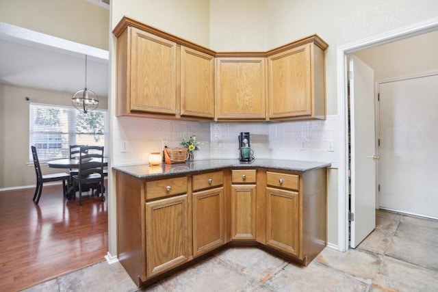 16710 Sabertooth Dr, Round Rock, TX 78681 - kitchen featuring a chandelier, backsplash, brown cabinets, dark stone countertops, and baseboards