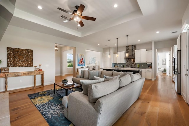 living area featuring recessed lighting, visible vents, baseboards, light wood-type flooring, and a raised ceiling