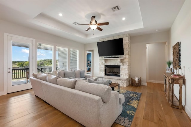 living area with a fireplace, a raised ceiling, visible vents, light wood-style floors, and a ceiling fan