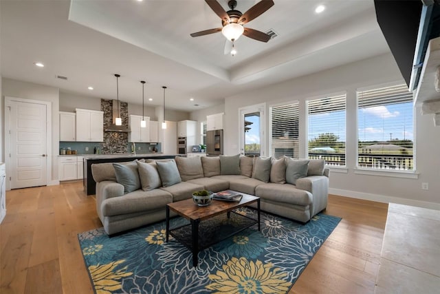 living room with baseboards, a raised ceiling, visible vents, and light wood-style floors