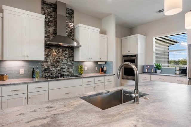 kitchen featuring black electric stovetop, visible vents, decorative backsplash, a sink, and wall chimney exhaust hood