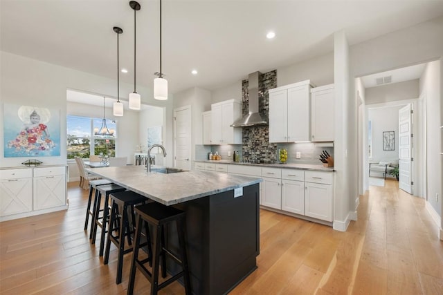 kitchen featuring tasteful backsplash, white cabinets, a sink, and wall chimney exhaust hood