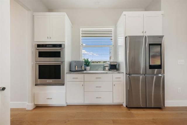 kitchen with light wood-style floors, baseboards, appliances with stainless steel finishes, and white cabinets