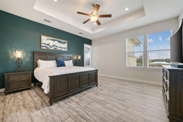 bedroom featuring light wood-type flooring, a raised ceiling, visible vents, and baseboards