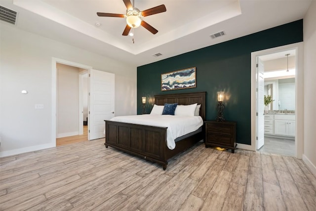 bedroom featuring light wood-style flooring, visible vents, and a raised ceiling