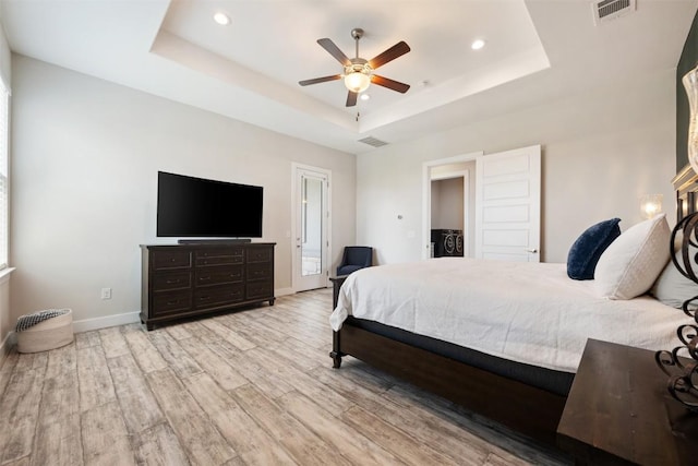 bedroom with a raised ceiling, visible vents, baseboards, and wood finished floors