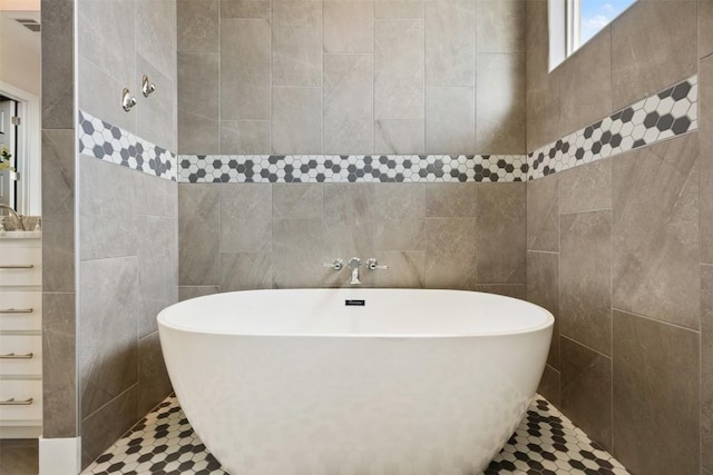 full bath with tile walls, visible vents, a sink, a tile shower, and a freestanding tub