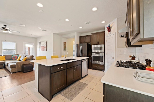 kitchen featuring dark brown cabinetry, visible vents, appliances with stainless steel finishes, a sink, and exhaust hood