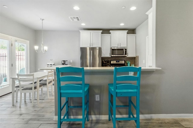 kitchen featuring a breakfast bar, visible vents, white cabinets, appliances with stainless steel finishes, and backsplash