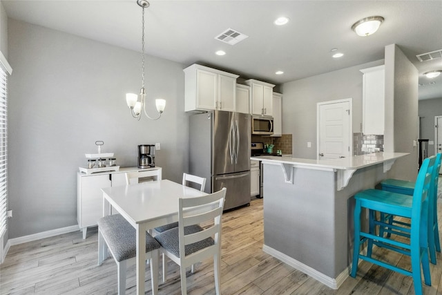 kitchen with tasteful backsplash, visible vents, light wood-style flooring, appliances with stainless steel finishes, and a breakfast bar