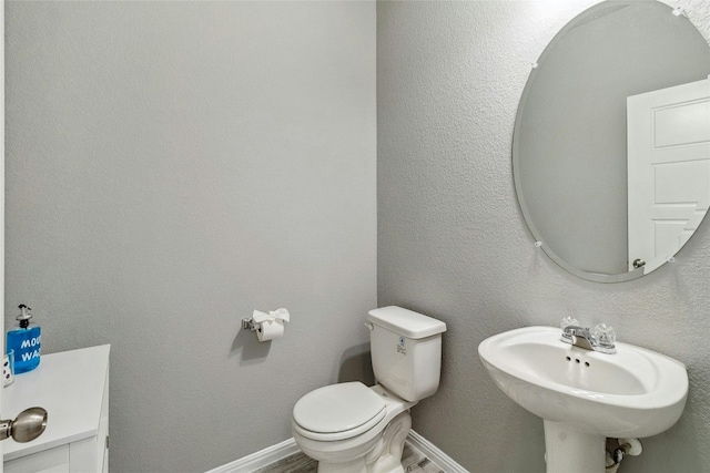 half bath featuring a textured wall, baseboards, a sink, and toilet