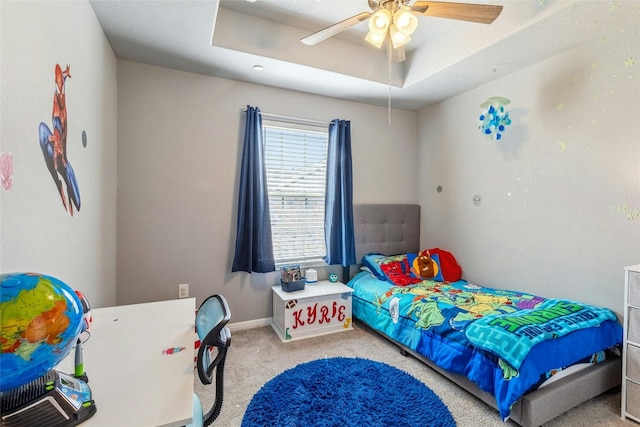 carpeted bedroom with baseboards, a raised ceiling, and a ceiling fan