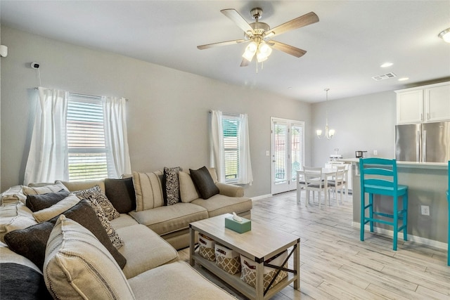 living room featuring light wood-style floors, visible vents, baseboards, and ceiling fan with notable chandelier