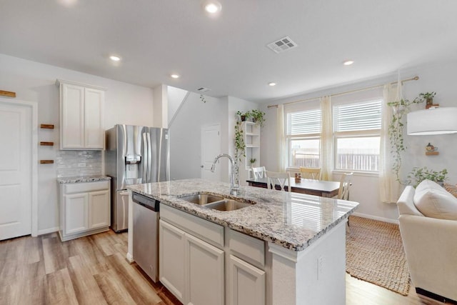 kitchen featuring visible vents, an island with sink, appliances with stainless steel finishes, a sink, and backsplash