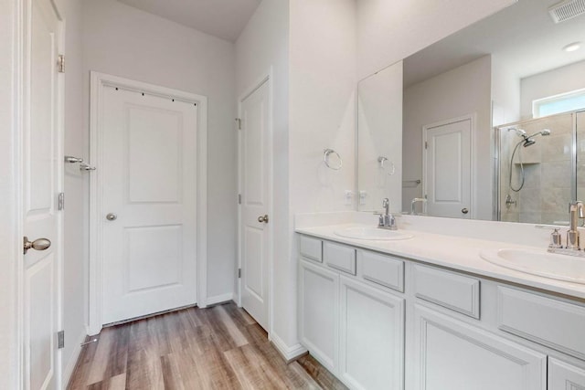 full bathroom with visible vents, a sink, a shower stall, and double vanity