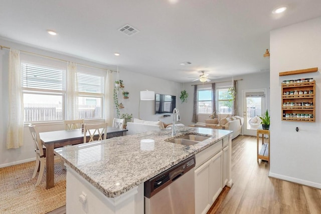 kitchen with light wood finished floors, visible vents, a kitchen island with sink, a sink, and dishwasher