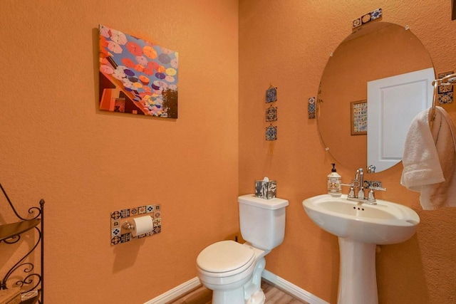 half bath with baseboards, toilet, and wood finished floors