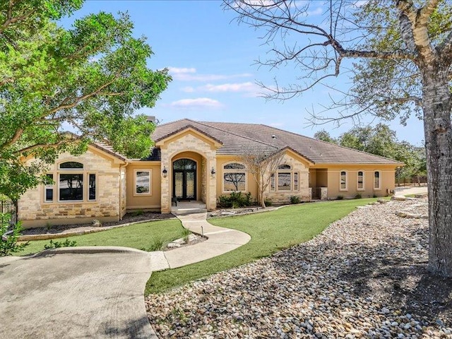 view of front of home with stone siding, a tiled roof, french doors, a front lawn, and stucco siding