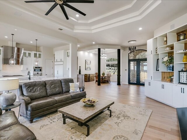 living area with a tray ceiling, recessed lighting, light wood-style floors, and ceiling fan with notable chandelier