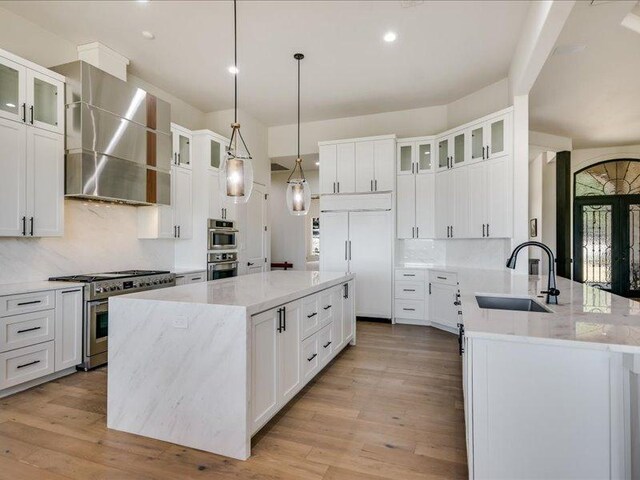kitchen with high end appliances, wall chimney range hood, light wood-style floors, and a sink