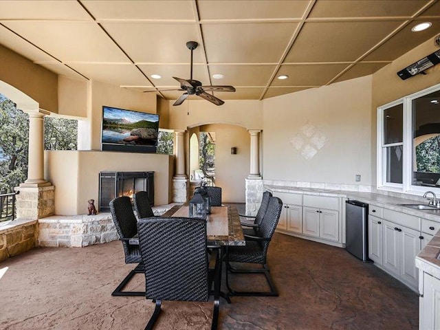 view of patio with ceiling fan, area for grilling, a sink, a lit fireplace, and outdoor dining space