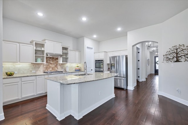 kitchen featuring arched walkways, open shelves, stainless steel appliances, backsplash, and a sink