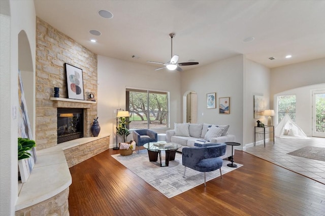 living area featuring arched walkways, a stone fireplace, and hardwood / wood-style floors