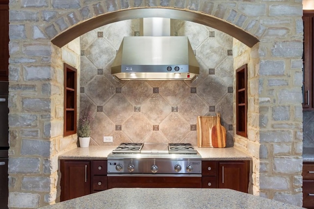 kitchen featuring stainless steel gas cooktop, wall chimney range hood, decorative backsplash, and light stone countertops