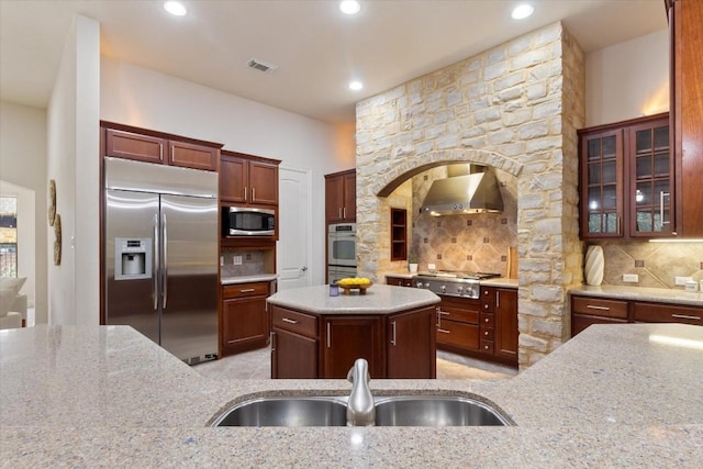 kitchen with visible vents, decorative backsplash, built in appliances, wall chimney range hood, and a sink