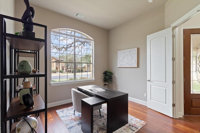 office space featuring baseboards, wood finished floors, visible vents, and a healthy amount of sunlight