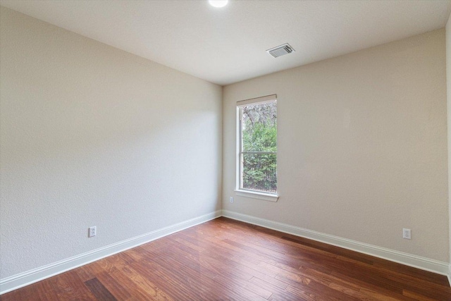 unfurnished room featuring baseboards, visible vents, and dark wood finished floors