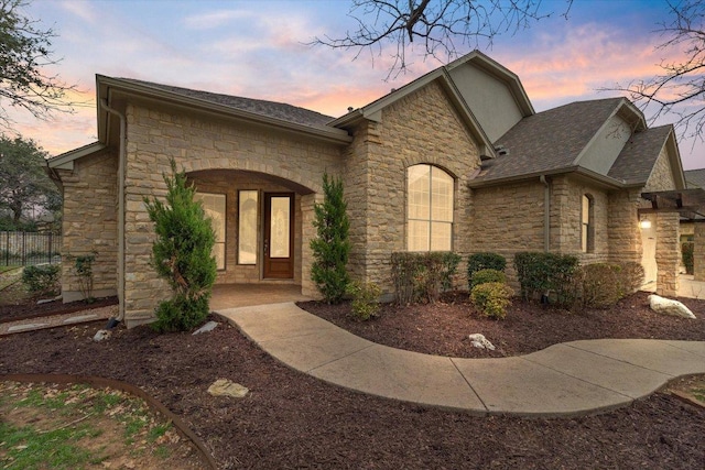 view of front of house featuring stone siding and roof with shingles