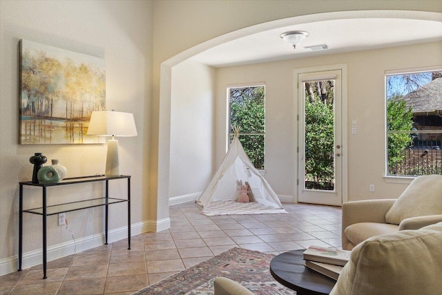 recreation room with arched walkways, a healthy amount of sunlight, visible vents, and tile patterned floors