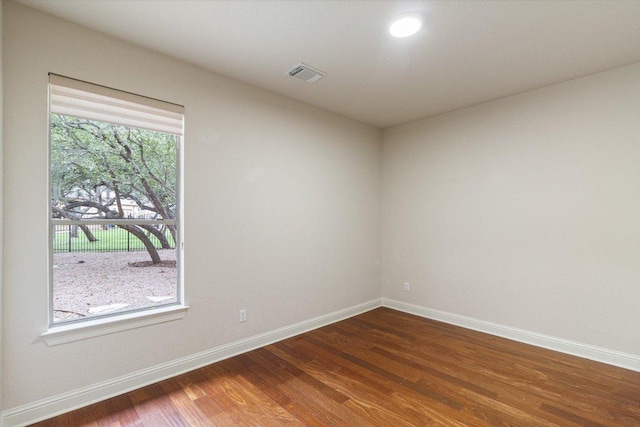 spare room with dark wood-style flooring, visible vents, and baseboards