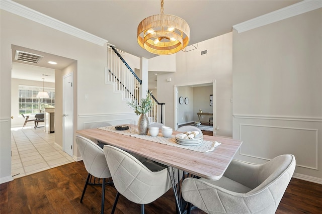 dining area with visible vents, dark wood-type flooring, stairs, crown molding, and a decorative wall