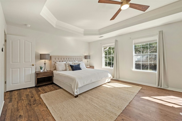 bedroom with dark wood-type flooring, a raised ceiling, ornamental molding, and baseboards