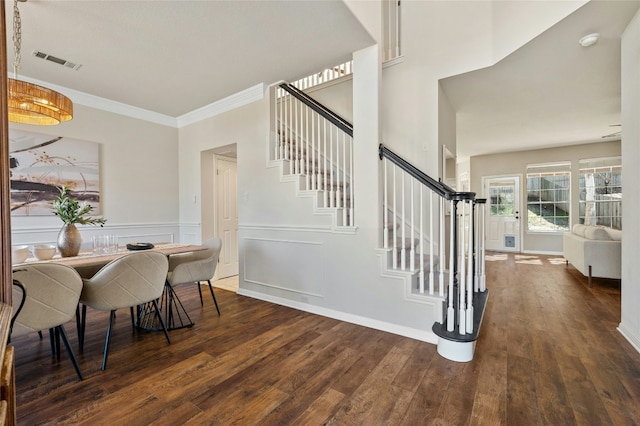 dining room featuring visible vents, ornamental molding, wainscoting, wood finished floors, and stairs