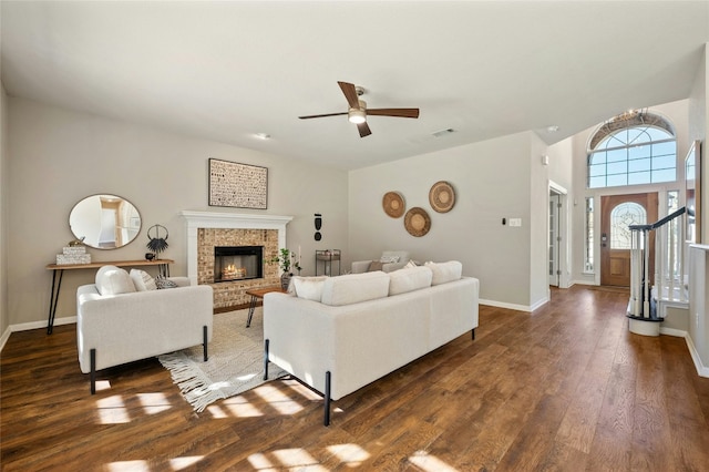 living room featuring a brick fireplace, visible vents, baseboards, and wood finished floors