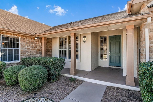 property entrance featuring stone siding, stucco siding, covered porch, and roof with shingles