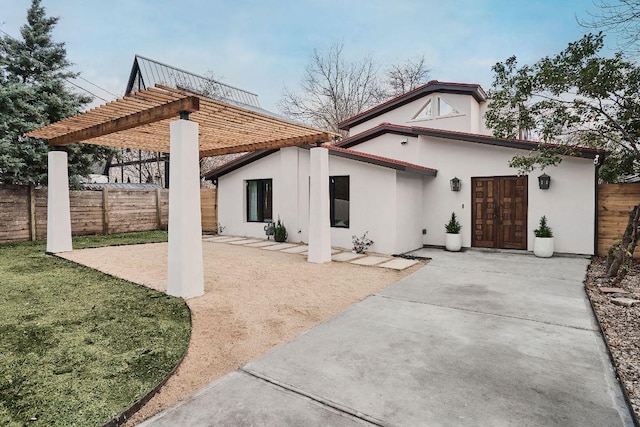 rear view of property featuring stucco siding, fence, a pergola, and a patio