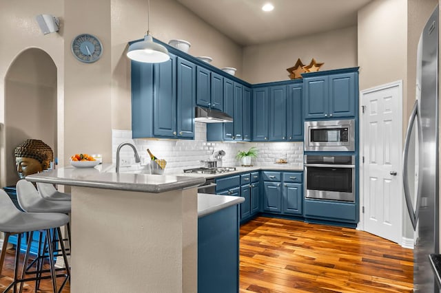 5312 Fort Benton Dr, Austin, TX 78735 - kitchen with stainless steel appliances, blue cabinets, a peninsula, under cabinet range hood, and wood finished floors