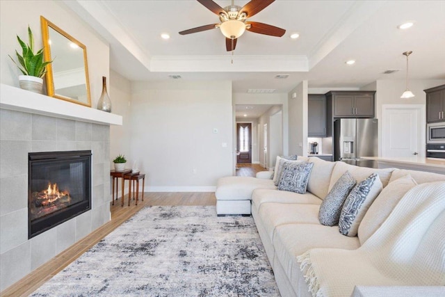 living room featuring a tile fireplace, light wood-type flooring, a raised ceiling, and baseboards