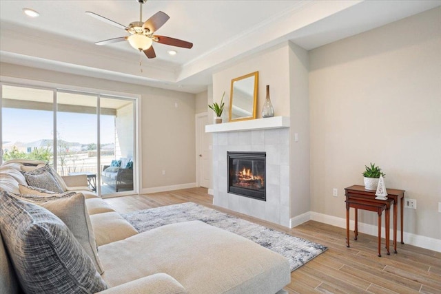 living room featuring light wood-style flooring, a fireplace, baseboards, a tray ceiling, and crown molding