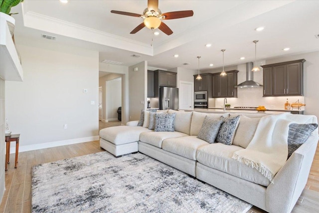 living area featuring light wood-style floors, a raised ceiling, visible vents, and baseboards