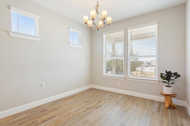 unfurnished room featuring an inviting chandelier, light wood-style flooring, and baseboards