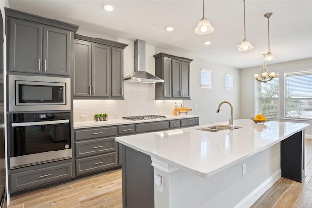 kitchen featuring a sink, appliances with stainless steel finishes, wood finish floors, and wall chimney range hood