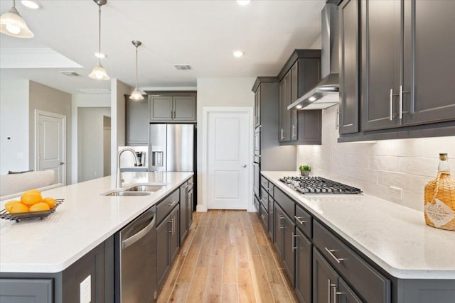 kitchen with stainless steel appliances, a sink, visible vents, backsplash, and wall chimney exhaust hood