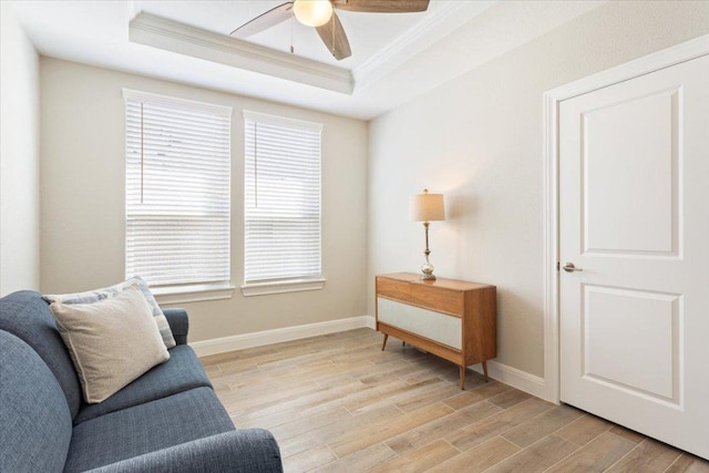 living area featuring crown molding, a raised ceiling, light wood-style floors, a ceiling fan, and baseboards